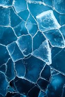 Cracked frozen lake surface with geometric pattern of broken ice pieces in deep blue tones, creating natural abstract texture for winter backgrounds.