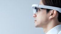 Young Asian man wearing futuristic smart glasses in profile view against light background, representing modern technology and augmented reality innovation.