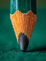 Extreme macro shot of pencil tip showing detailed wood texture and graphite point against emerald green background. Creative educational and artistic concept.