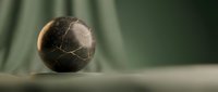 Cracked dark sphere with golden light reflection on neutral surface, suitable for abstract backgrounds and design projects.