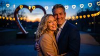 Happy mature couple embracing at romantic evening celebration with heart-shaped lights and warm bokeh background for anniversary or Valentine's Day.
