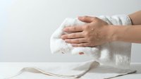 Hands gently drying white ceramic bowl with soft cotton towel in bright kitchen setting. Clean dishware care and household maintenance concept.