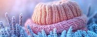 Cozy knitted winter hat with cable pattern resting on frost-covered evergreen branches in soft pastel light for seasonal fashion and cold weather accessories.