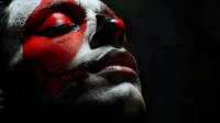 Dramatic close-up portrait with red face paint across eyes against dark background, highlighting intense artistic makeup and strong emotional expression. Perfect for theatrical design.