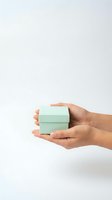 Hands gently holding small mint green gift box on clean white background for product presentation and commercial photography.