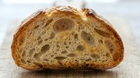 Freshly baked sourdough bread half showing open crumb structure and golden crust, ideal for bakery, food, and culinary design projects.
