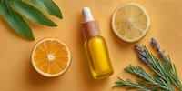 Natural citrus essential oil serum bottle with fresh orange lemon slices sage lavender herbs on warm orange background for skincare wellness aromatherapy products.
