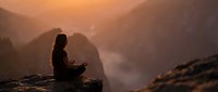 Young woman meditating in lotus position on mountain cliff during golden sunset with misty valley below, peaceful mindfulness and spiritual wellness concept.