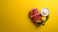 Raw ribeye steak with egg and spices on yellow background. Fresh beef cut ready for cooking with ingredients for seasoning and preparation.