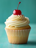 Vanilla cupcake with swirled cream frosting topped with red maraschino cherry on turquoise background for bakery menu and dessert advertising.