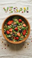 Fresh vegan salad with strawberries, walnuts, and greens in a wooden bowl, with the word vegan spelled out using edible flowers and herbs.
