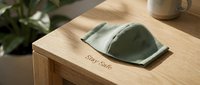 Green fabric face mask resting on a wooden table with Stay Safe text, soft natural light, health protection and safety concept.