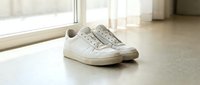 White leather sneakers on a light floor near a window, casual minimalist style, natural light, clean aesthetic for fashion and lifestyle concepts.