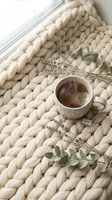 Cozy morning tea setup with herbal cup on chunky knit blanket decorated with dried lavender and eucalyptus branches creating peaceful hygge atmosphere.