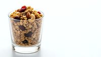 Homemade granola with nuts and dried cranberries in glass cup on white background, healthy breakfast cereal mix for morning meal preparation.