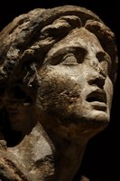Ancient stone sculpture of woman's head with weathered features and flowing hair carved in classical style against dark background for historical projects.