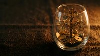 Golden coins falling into transparent glass on textured surface with warm lighting creating wealth and prosperity concept for financial investment themes.