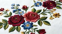 Embroidered floral pattern with red roses and blue flowers on white fabric. Traditional needlework design for textile decoration and craft projects.