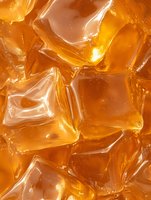 Golden amber ice cubes with glossy translucent surface creating refreshing beverage background for summer drinks and cocktail photography.