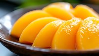 Fresh sliced yellow peaches arranged in a curved row on dark ceramic plate, macro food photography showing juicy fruit texture and natural lighting.