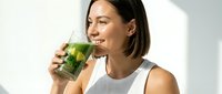 Young woman with dark hair and olive complexion drinking fresh green juice or smoothie from glass, wellness and healthy lifestyle concept.