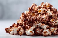 Chocolate-covered popcorn heap on light background, sweet and savory snack for movie night or party treats.