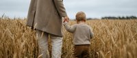 Father and young son walking hand in hand through golden wheat field on overcast day, family bonding moment in rural countryside setting.