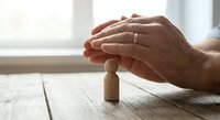 Hands protecting wooden figure symbolizing care, insurance, safety and security concept for business presentations and healthcare materials.