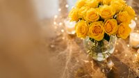 Fresh yellow roses bouquet in glass vase with warm bokeh lights creating romantic atmosphere for celebrations, weddings, anniversaries and special occasions.