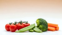 Fresh organic vegetables including cherry tomatoes on vine, snap peas, broccoli and carrots arranged on white background for healthy cooking and nutrition.
