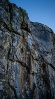 Weathered limestone cliff face with natural erosion patterns and lichen growth against clear blue sky for outdoor adventure and geological concepts.