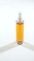 Glass spray bottle with golden yellow liquid isolated on white background for cosmetic and skincare product photography.