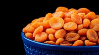 Fresh dried apricots in blue ceramic bowl on black background, bright orange color contrast, healthy natural snack for nutritious eating and cooking.