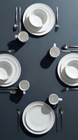Overhead view of four place settings with white dinnerware, cups, and metallic cutlery arranged on dark gray surface with dramatic shadows for dining and hospitality design.