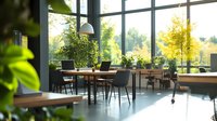 Modern coworking space with wooden tables, gray chairs, and abundant natural light from floor-to-ceiling windows overlooking lush green trees and nature.