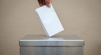 Hand placing white ballot into gray voting box during election process for democratic participation and civic duty.