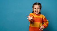 Happy young girl in colorful striped sweater reaching out hand with welcoming gesture on blue background for children clothing and lifestyle concepts.