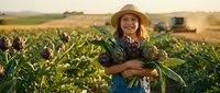 Young female farmer holding fresh corn harvest in agricultural field during golden hour sunset with farming equipment in background.