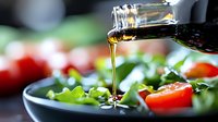 Pouring olive oil dressing over fresh green salad with cherry tomatoes, captured in dynamic motion with natural lighting and shallow depth of field.