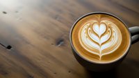 Coffee cup with heart latte art on wooden table surface perfect for cafe menu design and coffee shop marketing materials.