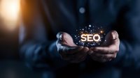 Male hands holding glowing SEO text with sparkle effects against dark background, representing digital marketing and search engine optimization concepts in business setting.