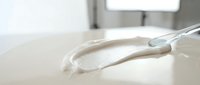 White cream or lotion being squeezed from silver tube onto clean surface in bright modern bathroom setting for skincare and cosmetic product advertising.