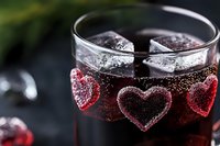 Romantic red cocktail with heart shaped ice cubes and bubbles in glass on dark background. Close up view of refreshing Valentine's Day drink garnish.