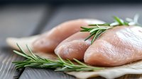 Raw chicken breast fillets with fresh rosemary herbs on wooden cutting board ready for cooking and meal preparation in modern kitchen setting.
