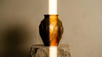 Metallic bronze decorative vase with embossed leaf pattern sitting on stone pedestal, illuminated by warm light for home decor and interior design projects.
