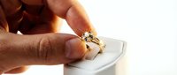 Hand holding a gold diamond engagement ring above a white jewelry box, close-up shot for wedding, luxury, and retail concepts.