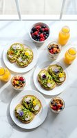 Healthy breakfast spread with avocado toast topped with edible flowers, fresh berries, granola parfait and orange juice on marble table for morning meal.