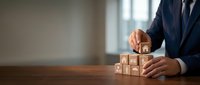 Professional businessman in dark suit arranging wooden blocks with question marks on office desk, representing problem-solving and decision-making concepts.