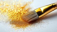 Golden glitter powder scattered on white surface with professional makeup brush featuring metallic gold ferrule, creating luxurious cosmetic composition.