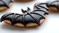 Black bat-shaped Halloween cookies with dark chocolate icing on white background, homemade spooky treats for holiday party and seasonal celebration.